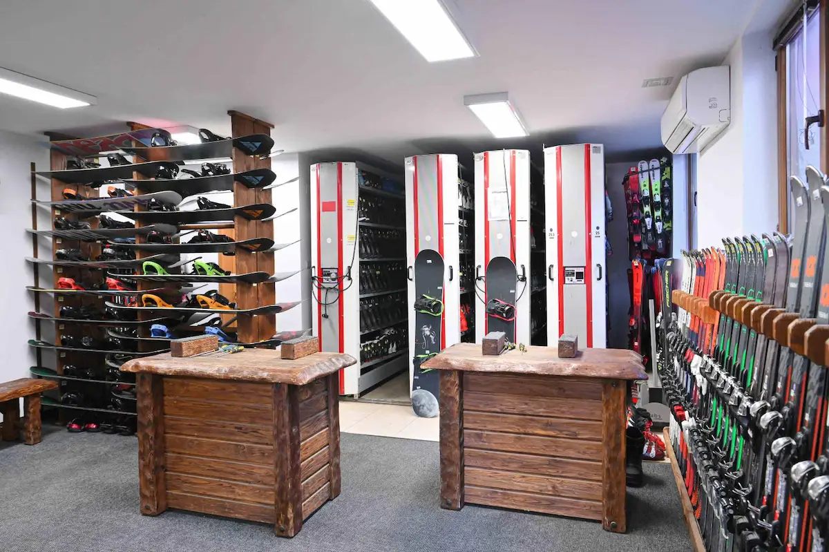 Interior of a Bansko ski rental shop showing rustic wooden workbenches, wall-mounted racks of skis and snowboards, and tall red-and-white storage lockers for boots and gear.